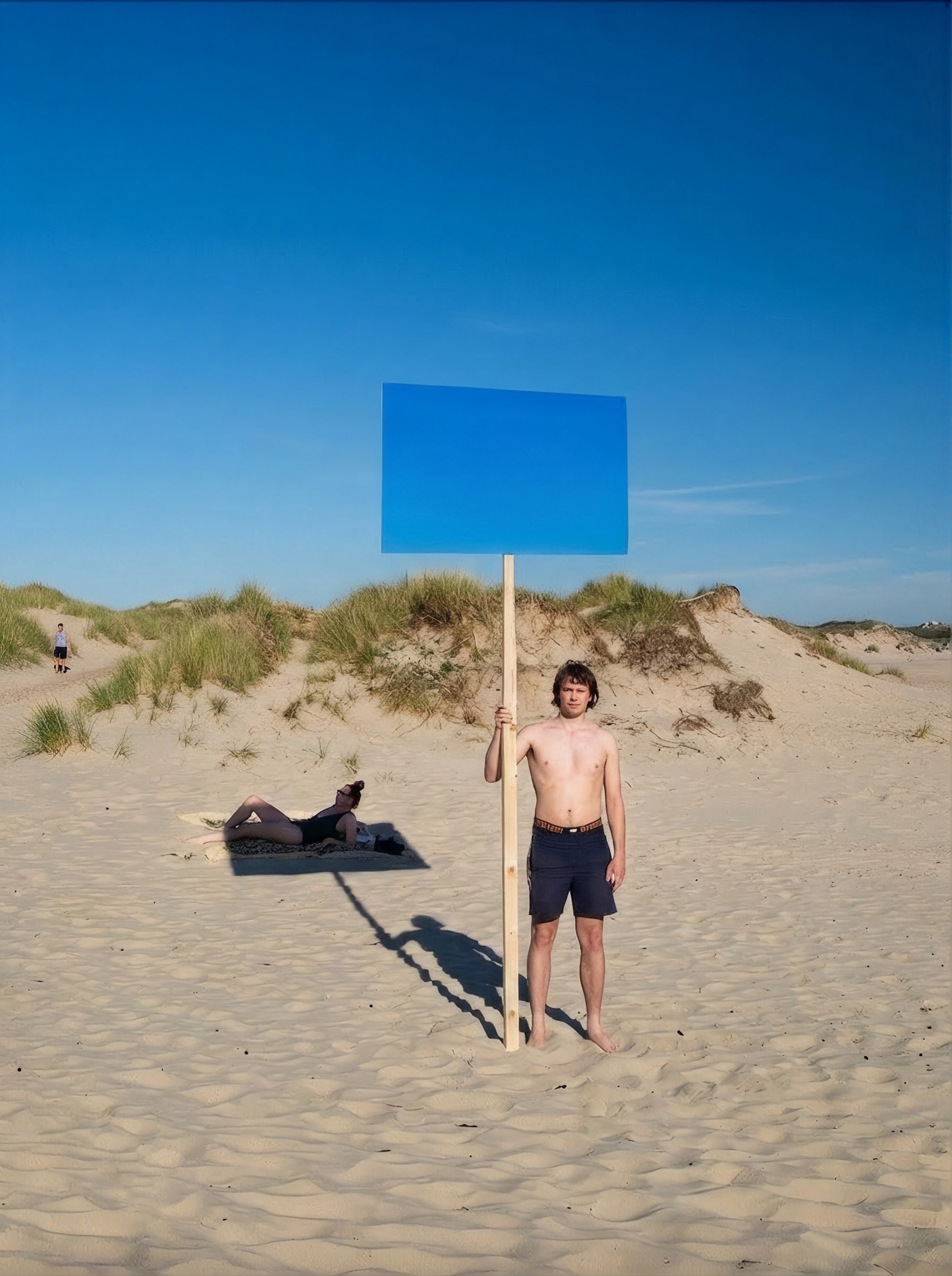 A man on a sand dune holding up a blank blue sign